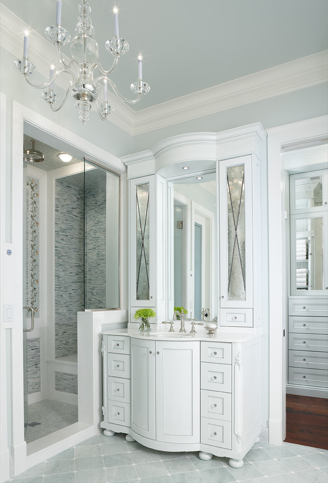 Modelo de cuarto de baño principal clásico con puertas de armario blancas, ducha empotrada, baldosas y/o azulejos grises, paredes azules, lavabo bajoencimera, encimera de acrílico y armarios con paneles empotrados