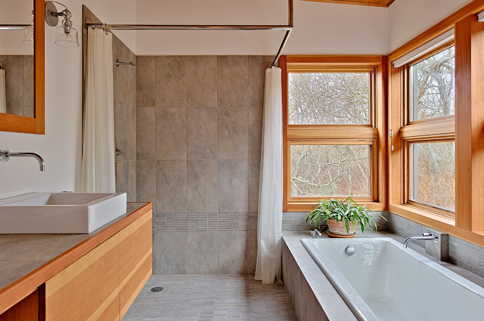 Inspiration for a small modern ensuite bathroom in Seattle with a vessel sink, flat-panel cabinets, light wood cabinets, white walls, ceramic flooring, a built-in bath, a walk-in shower, grey tiles, ceramic tiles, tiled worktops, grey floors, a shower curtain and grey worktops.