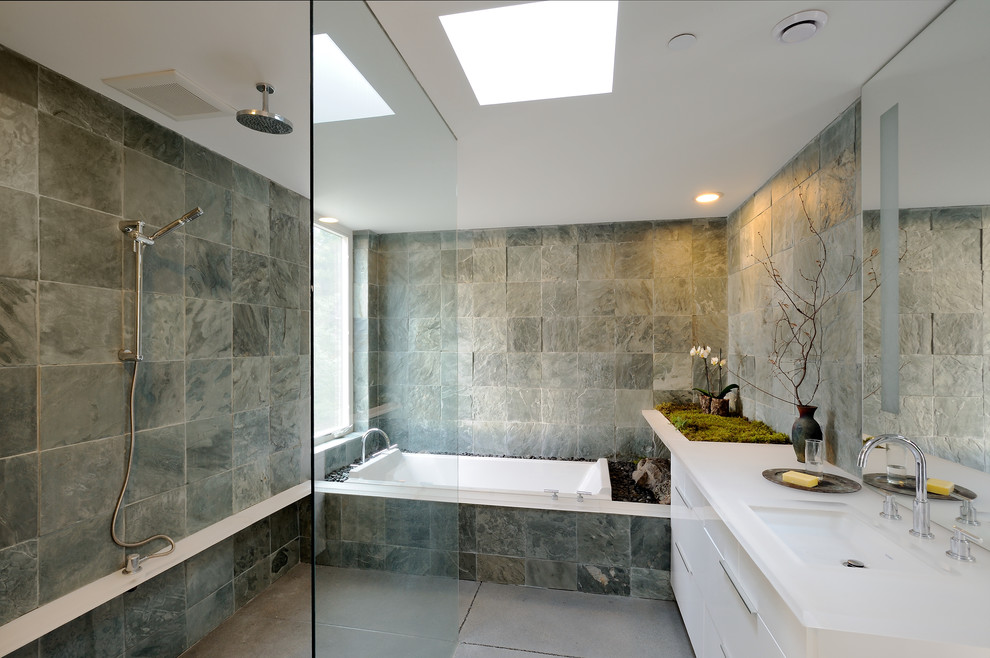 Inredning av ett modernt mellanstort en-suite badrum, med ett badkar i en alkov, grå kakel, grå väggar, en kantlös dusch, släta luckor, vita skåp, en toalettstol med hel cisternkåpa, betonggolv, bänkskiva i akrylsten, ett undermonterad handfat och skifferkakel