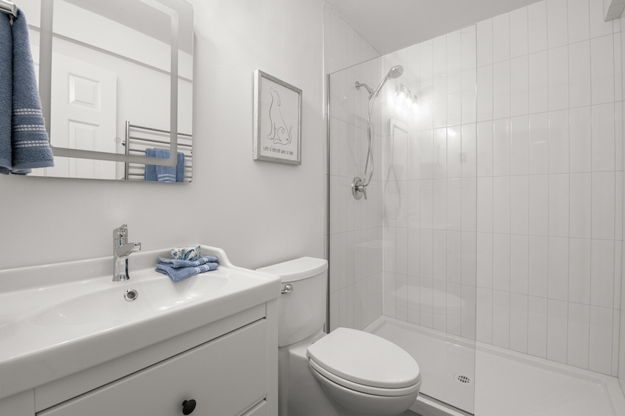 Klassisk inredning av ett litet vit vitt badrum med dusch, med släta luckor, vita skåp, en öppen dusch, en toalettstol med separat cisternkåpa, vit kakel, porslinskakel, klinkergolv i porslin och grått golv