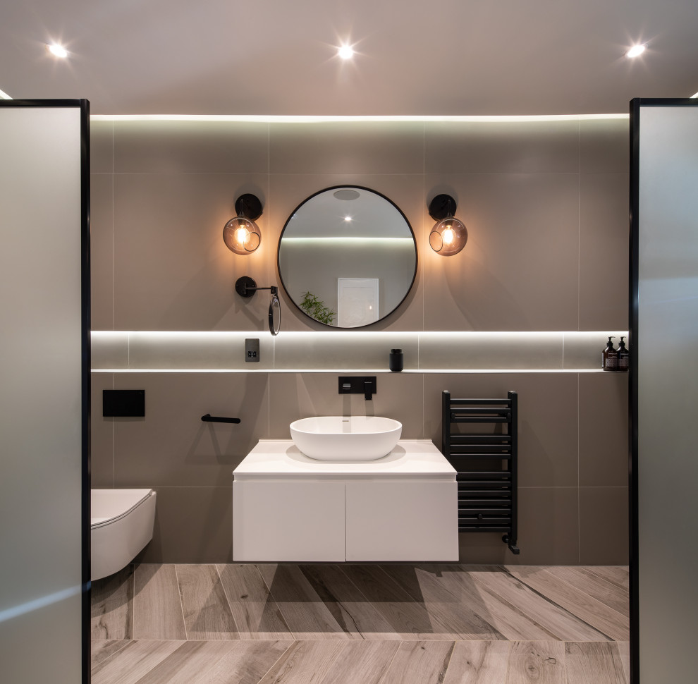 Trendy master gray tile and porcelain tile porcelain tile and gray floor bathroom photo in London with flat-panel cabinets, white cabinets, a wall-mount toilet, gray walls, a vessel sink, solid surface countertops and white countertops
