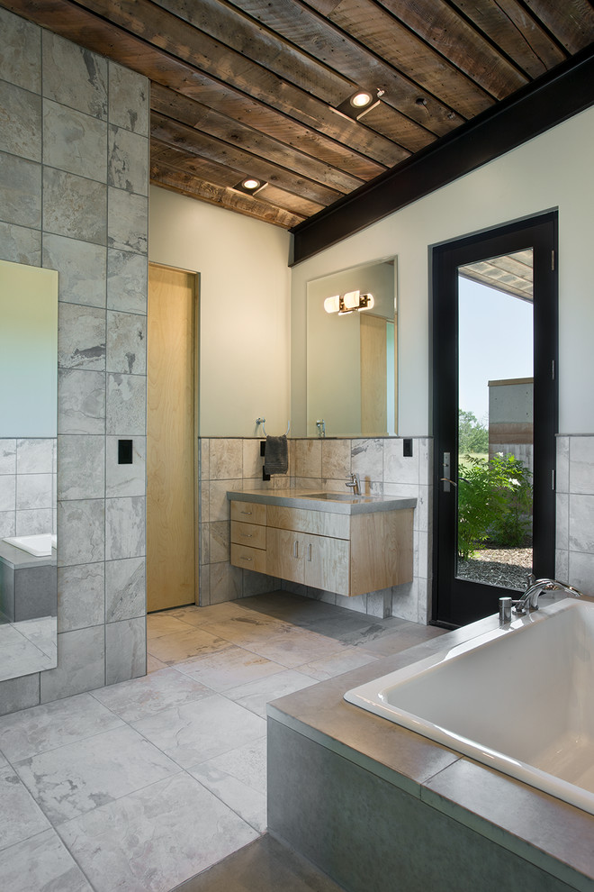 Imagen de cuarto de baño actual con puertas de armario de madera clara, bañera empotrada y baldosas y/o azulejos grises