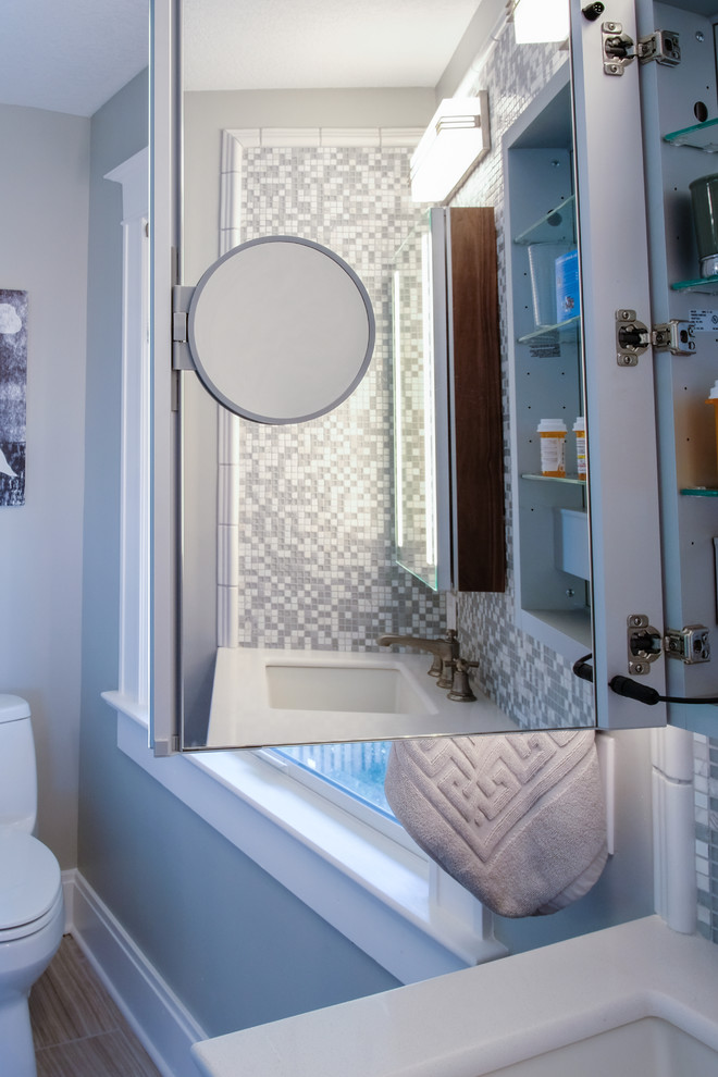 На фото: ванная комната среднего размера в стиле неоклассика (современная классика) с фасадами с утопленной филенкой, темными деревянными фасадами, угловым душем, унитазом-моноблоком, белой плиткой, керамогранитной плиткой, серыми стенами, полом из ламината, душевой кабиной, врезной раковиной, столешницей из искусственного кварца, коричневым полом, душем с распашными дверями и белой столешницей с