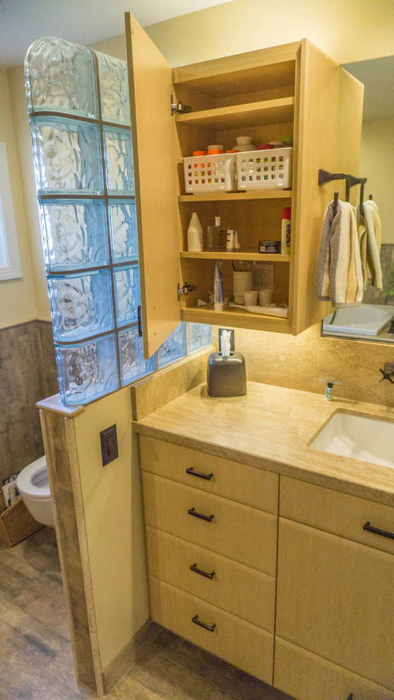 Cette image montre une salle de bain principale bohème en bois clair de taille moyenne avec un placard à porte plane, une baignoire posée, WC suspendus, un mur jaune, un sol en carrelage de porcelaine, un lavabo encastré et un plan de toilette en marbre.