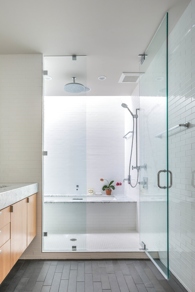 На фото: ванная комната в современном стиле с плоскими фасадами, фасадами цвета дерева среднего тона, душем над ванной, белой плиткой и белыми стенами с