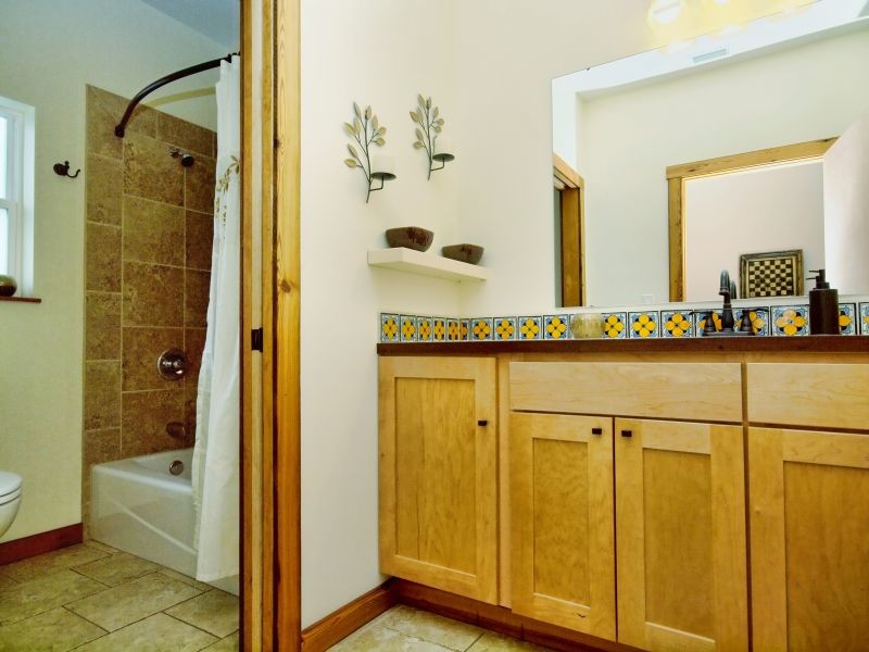 オースティンにある中くらいなコンテンポラリースタイルのおしゃれなバスルーム (浴槽なし) (アンダーカウンター洗面器、シェーカースタイル扉のキャビネット、淡色木目調キャビネット、コーナー型浴槽、シャワー付き浴槽	、一体型トイレ	、ベージュのタイル、セラミックタイル、白い壁、セラミックタイルの床) の写真