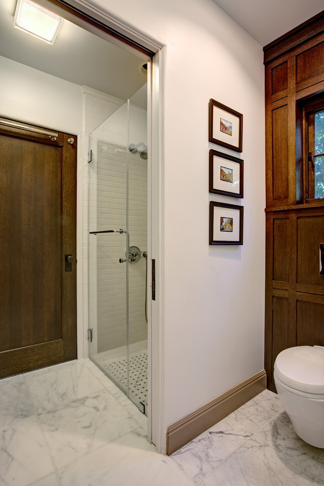 Inspiration for a small timeless 3/4 white tile and stone tile marble floor, white floor and wood wall walk-in shower remodel in San Francisco with shaker cabinets, dark wood cabinets, a wall-mount toilet, brown walls, an undermount sink, solid surface countertops and a hinged shower door