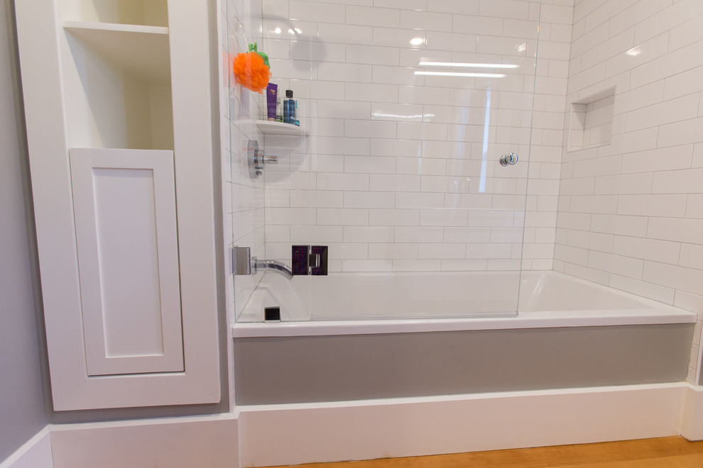 Photo of a small contemporary ensuite bathroom in Boston with flat-panel cabinets, white cabinets, an alcove bath, an alcove shower, a one-piece toilet, white tiles, metro tiles, grey walls, medium hardwood flooring, an integrated sink, solid surface worktops, brown floors and a sliding door.