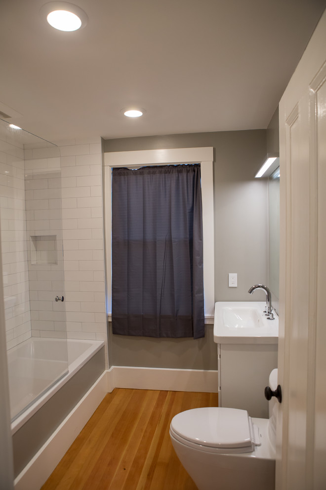 Exempel på ett litet modernt en-suite badrum, med vita skåp, ett badkar i en alkov, en dusch i en alkov, en toalettstol med hel cisternkåpa, vit kakel, tunnelbanekakel, grå väggar, mellanmörkt trägolv, ett integrerad handfat, bänkskiva i akrylsten, brunt golv, dusch med skjutdörr och släta luckor