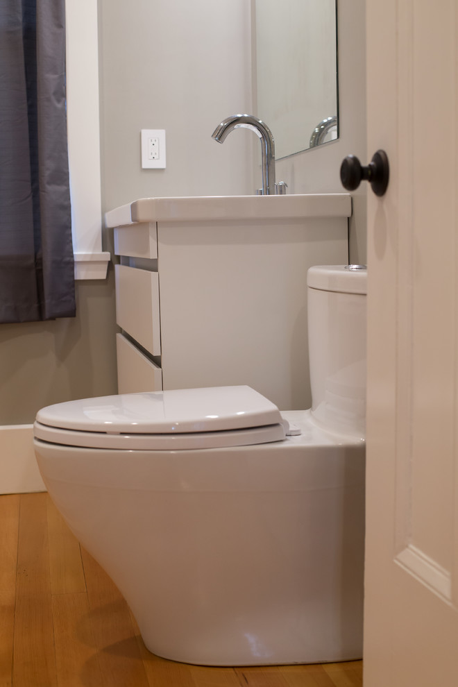 Design ideas for a small contemporary ensuite bathroom in Boston with flat-panel cabinets, white cabinets, an alcove bath, an alcove shower, a one-piece toilet, white tiles, metro tiles, grey walls, medium hardwood flooring, an integrated sink, solid surface worktops, brown floors and a sliding door.