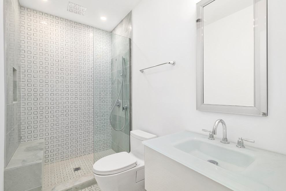 ニューヨークにあるコンテンポラリースタイルのおしゃれな浴室 (一体型トイレ	、白い壁、オープンシャワー、白い洗面カウンター、フラットパネル扉のキャビネット、白いキャビネット、アルコーブ型シャワー、白いタイル、一体型シンク、ガラスの洗面台、白い床) の写真