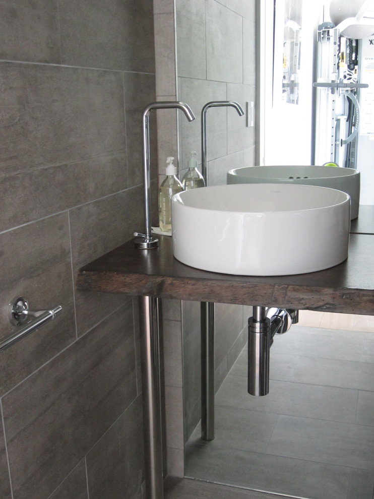 Foto di una stanza da bagno minimalista con lavabo a bacinella, top in legno, WC sospeso e piastrelle grigie