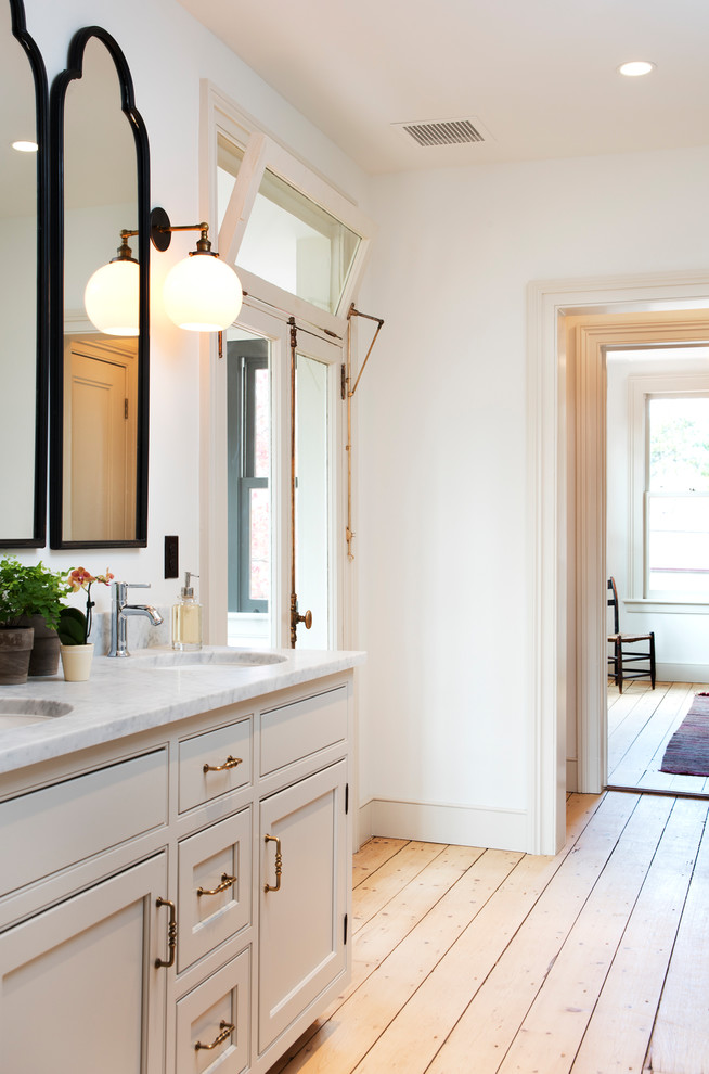 Klassisches Badezimmer mit Schrankfronten mit vertiefter Füllung, beigen Schränken, weißer Wandfarbe, hellem Holzboden, Unterbauwaschbecken, braunem Boden und grauer Waschtischplatte in New York