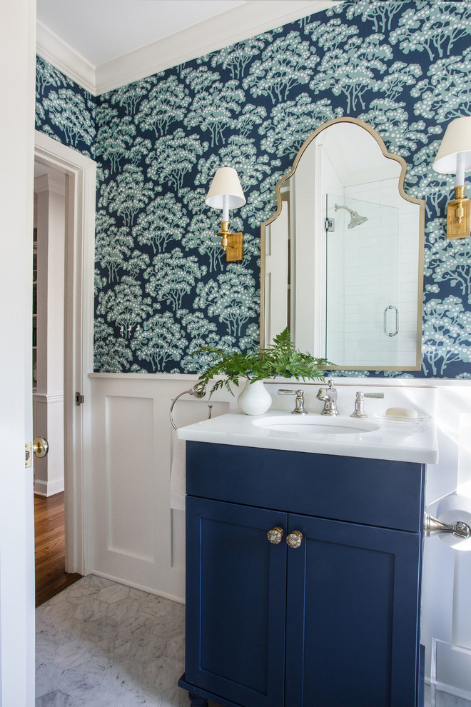 Cette photo montre une salle de bain chic avec un placard à porte shaker, des portes de placard bleues, WC séparés, un lavabo encastré, un plan de toilette en marbre, un sol blanc, un plan de toilette blanc et un mur bleu.