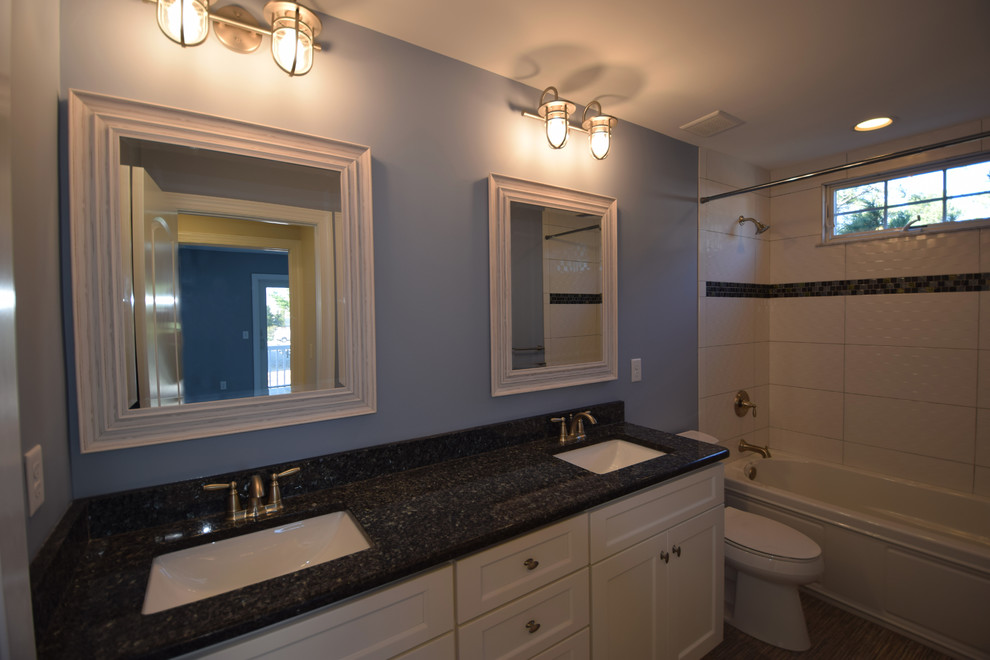 Maritim inredning av ett badrum, med luckor med infälld panel, vita skåp, en dusch/badkar-kombination, vit kakel, blå väggar, klinkergolv i keramik och ett undermonterad handfat