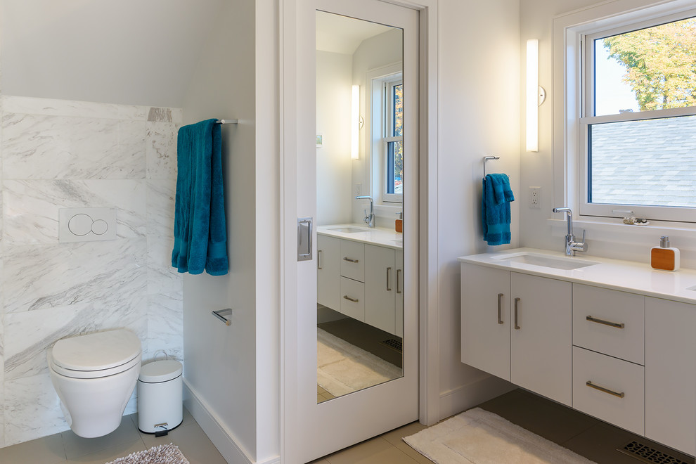 Bild på ett mellanstort funkis vit vitt en-suite badrum, med släta luckor, vita skåp, en dusch i en alkov, vit kakel, marmorkakel, vita väggar, klinkergolv i porslin, ett undermonterad handfat, bänkskiva i kvarts, grått golv, dusch med gångjärnsdörr och en vägghängd toalettstol