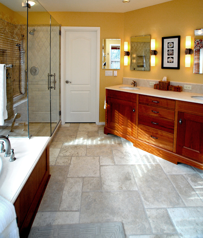 На фото: большая главная ванная комната в классическом стиле с фасадами в стиле шейкер, фасадами цвета дерева среднего тона, ванной в нише, угловым душем, бежевой плиткой, каменной плиткой, желтыми стенами, полом из известняка, врезной раковиной и столешницей из известняка с