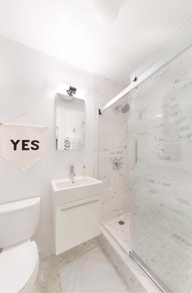 This is an example of a small modern ensuite bathroom in New York with a wall-mounted sink, a corner shower, a one-piece toilet, white tiles, stone tiles, white walls and ceramic flooring.