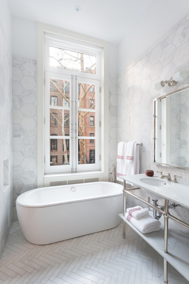 Medium sized contemporary ensuite bathroom in New York with a built-in sink, marble worktops, a freestanding bath, white tiles, ceramic tiles, white walls, ceramic flooring, a corner shower, a hinged door and grey floors.