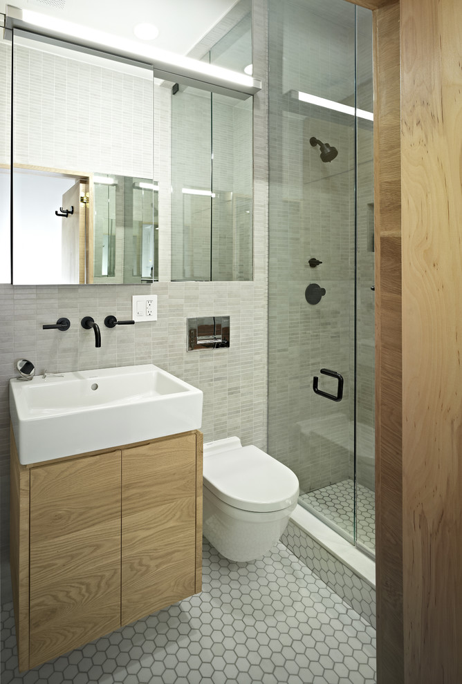 Trendy gray tile alcove shower photo in New York with a wall-mount sink, flat-panel cabinets, a wall-mount toilet and light wood cabinets