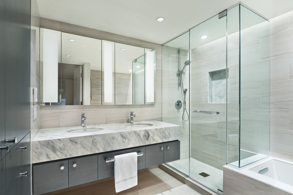 Small contemporary ensuite bathroom in New York with a submerged sink, flat-panel cabinets, grey cabinets, marble worktops, a submerged bath, a corner shower, beige tiles, stone tiles, beige walls and ceramic flooring.
