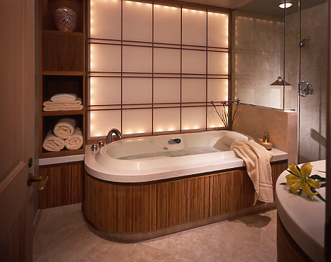 Modelo de cuarto de baño principal asiático de tamaño medio con armarios tipo mueble, puertas de armario de madera oscura, bañera encastrada, ducha empotrada, baldosas y/o azulejos beige, baldosas y/o azulejos de piedra, lavabo integrado y encimera de acrílico