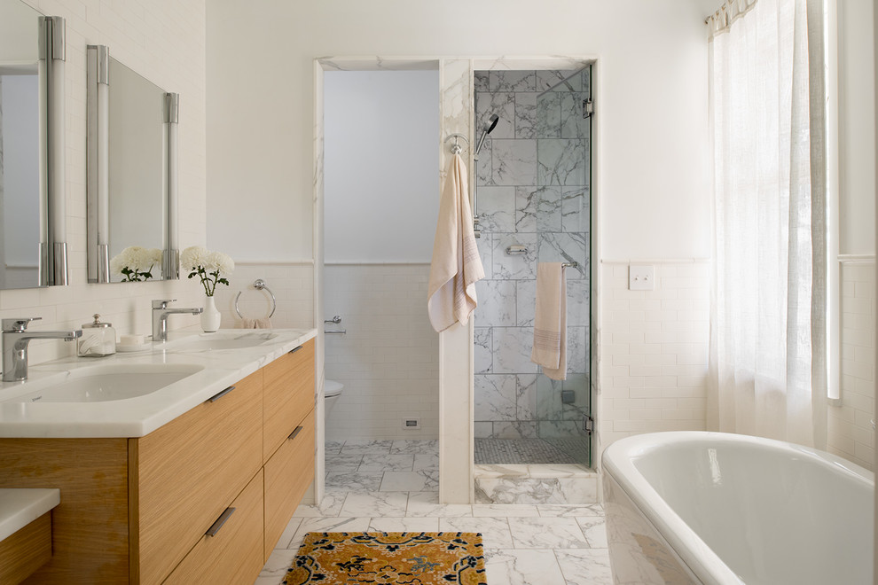 Inredning av ett klassiskt badrum, med släta luckor, skåp i mellenmörkt trä, ett fristående badkar, en dusch i en alkov, vit kakel, tunnelbanekakel, vita väggar, ett undermonterad handfat och dusch med gångjärnsdörr