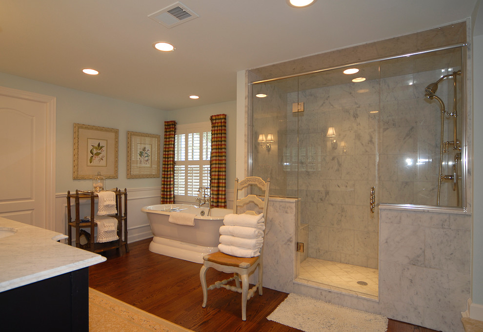 Ejemplo de cuarto de baño principal clásico grande con armarios tipo mueble, puertas de armario negras, bañera exenta, suelo de madera oscura y encimera de mármol