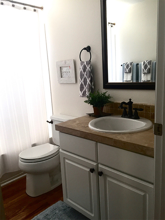 Klassisk inredning av ett litet badrum, med luckor med upphöjd panel, vita skåp, en dusch/badkar-kombination, en toalettstol med separat cisternkåpa, vita väggar, mörkt trägolv och ett nedsänkt handfat