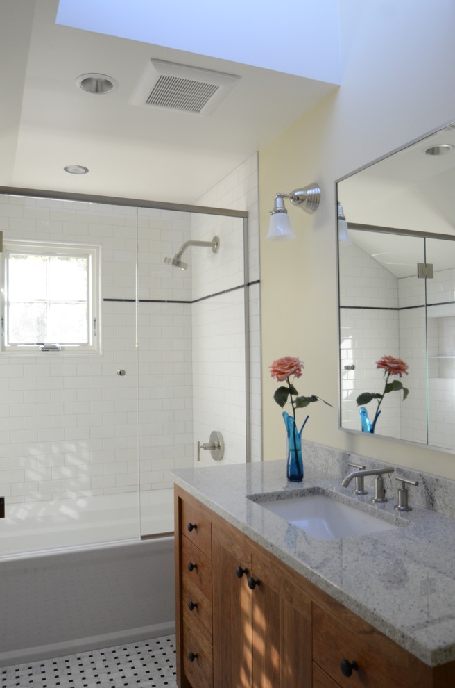 Aménagement d'une salle de bain classique en bois clair avec un lavabo encastré, une baignoire en alcôve, un combiné douche/baignoire, un plan de toilette en granite, un carrelage blanc et un carrelage métro.