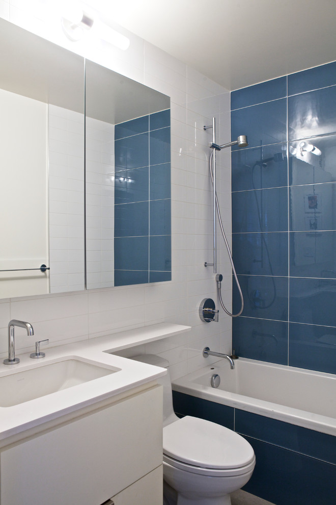 Пример оригинального дизайна: маленькая ванная комната в современном стиле с плоскими фасадами, белыми фасадами, ванной в нише, унитазом-моноблоком, синей плиткой, стеклянной плиткой, белыми стенами, полом из керамогранита, душевой кабиной, врезной раковиной и столешницей из искусственного кварца для на участке и в саду