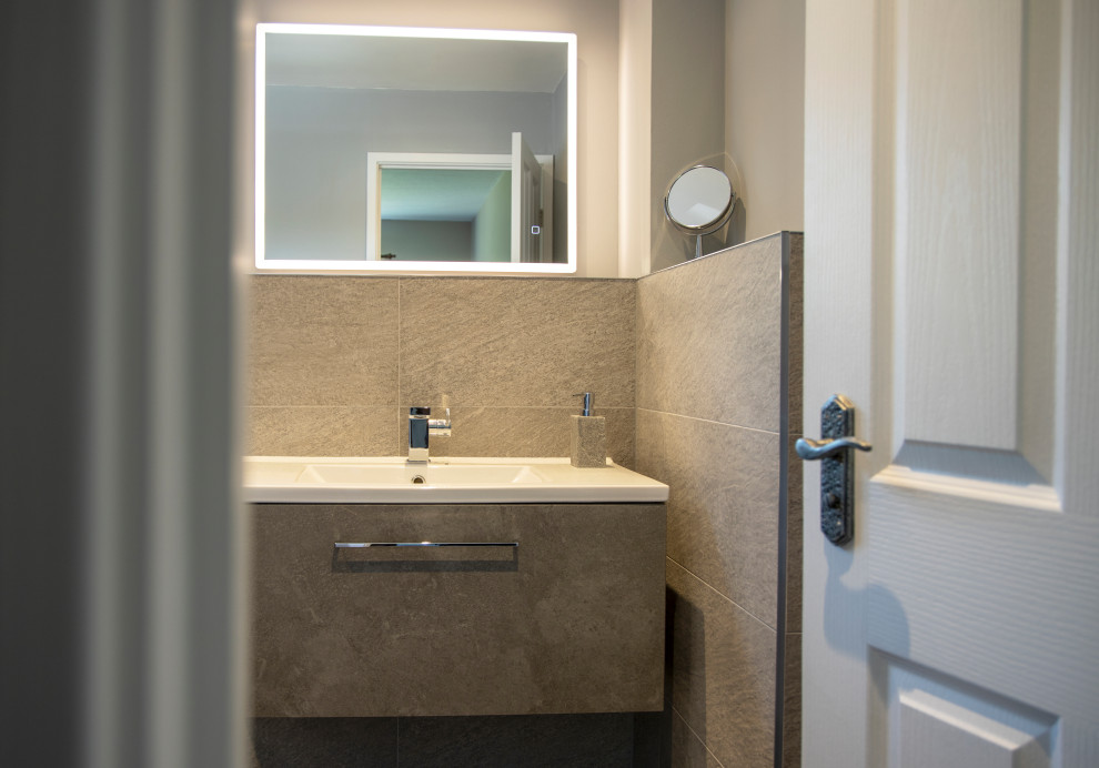 Foto på ett mellanstort funkis en-suite badrum, med grå skåp, en öppen dusch, en toalettstol med hel cisternkåpa, grå kakel, porslinskakel, beige väggar, klinkergolv i porslin, ett väggmonterat handfat, grått golv, med dusch som är öppen och släta luckor