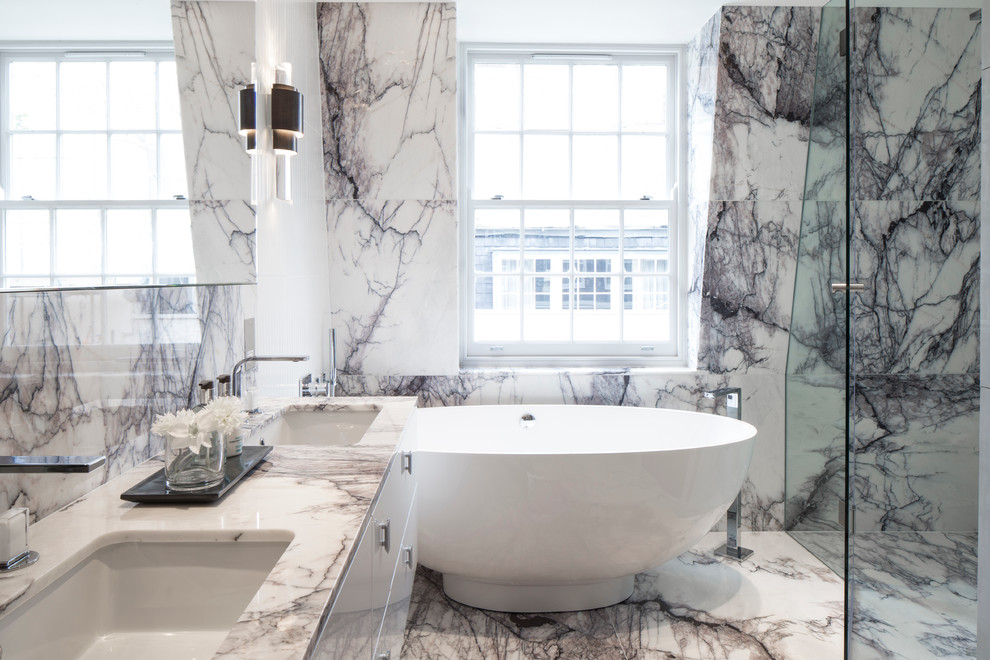 Cette image montre une salle de bain traditionnelle avec un lavabo encastré, un placard à porte plane, des portes de placard blanches, un plan de toilette en marbre, une baignoire indépendante, une douche d'angle, un mur gris et un sol en marbre.
