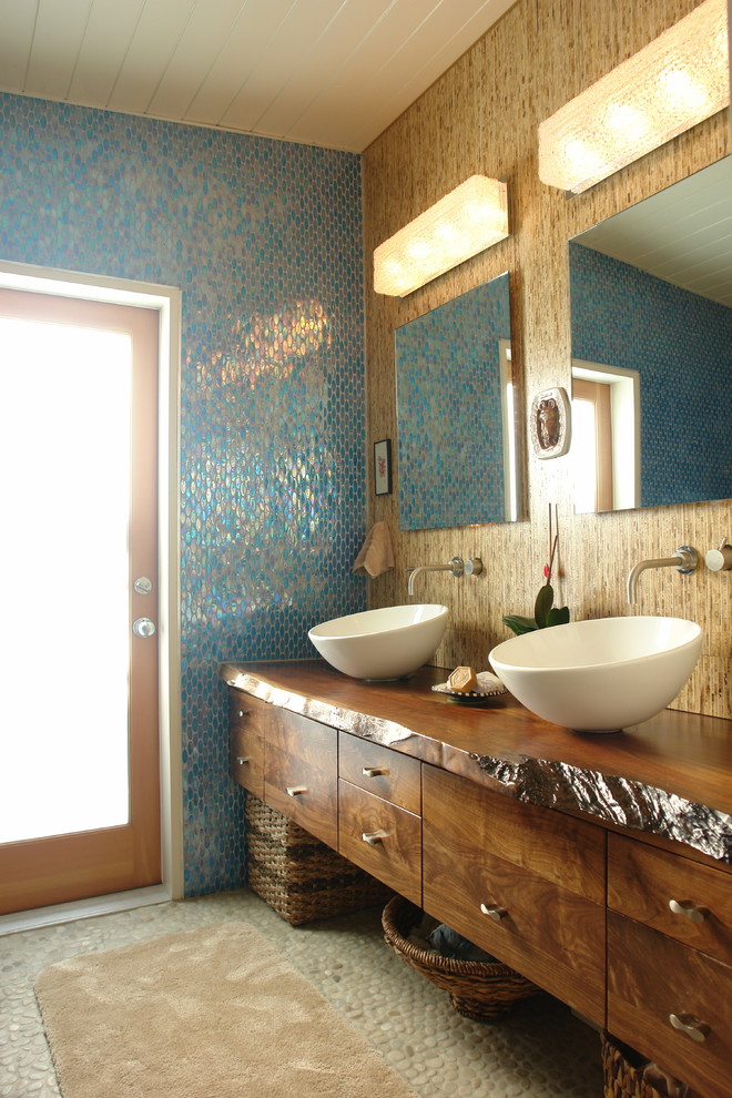 Bild på ett stort tropiskt en-suite badrum, med skåp i mörkt trä, träbänkskiva, blå kakel, ett fristående handfat, klinkergolv i småsten, släta luckor, glaskakel och bruna väggar
