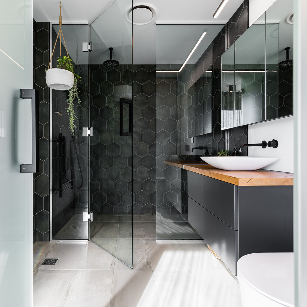 Bild på ett funkis brun brunt badrum med dusch, med släta luckor, svarta skåp, en kantlös dusch, svart kakel, vita väggar, ett fristående handfat, träbänkskiva, grått golv och dusch med gångjärnsdörr