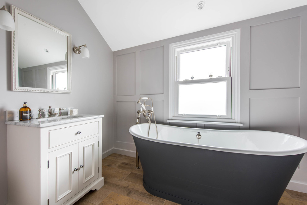 Classic bathroom in London with beaded cabinets, white cabinets, a freestanding bath, grey walls, light hardwood flooring and a submerged sink.
