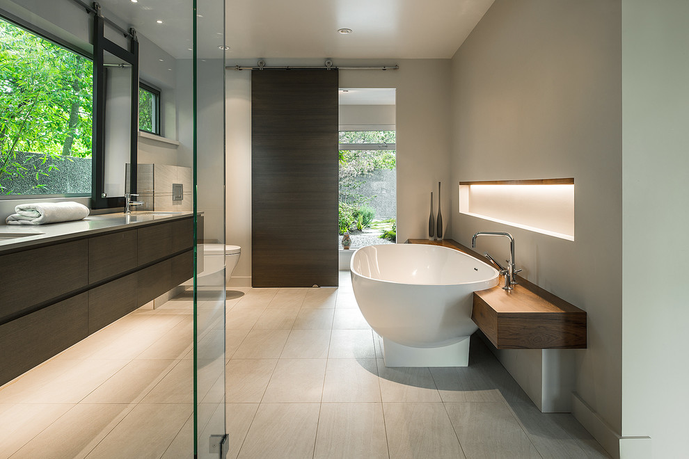 Стильный дизайн: ванная комната среднего размера в современном стиле с врезной раковиной, плоскими фасадами, темными деревянными фасадами, отдельно стоящей ванной, душем без бортиков, инсталляцией, бежевой плиткой и белыми стенами - последний тренд