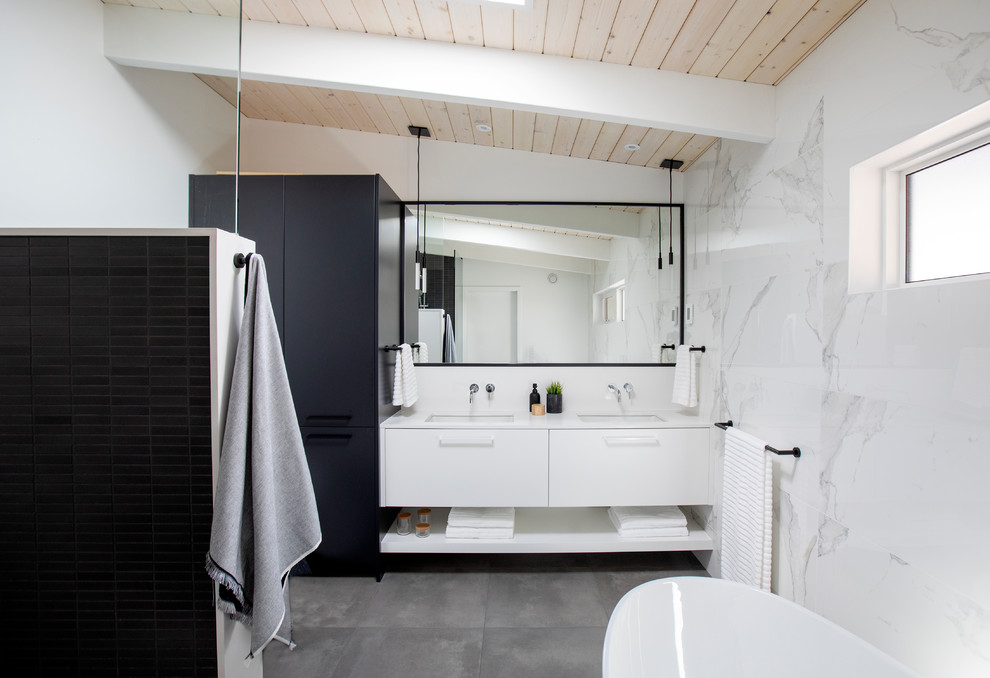 Пример оригинального дизайна: главная ванная комната среднего размера в стиле ретро с плоскими фасадами, белыми фасадами, белой плиткой, мраморной плиткой, белыми стенами, врезной раковиной, серым полом, белой столешницей, бетонным полом, столешницей из искусственного кварца, отдельно стоящей ванной, душем без бортиков, открытым душем и зеркалом с подсветкой