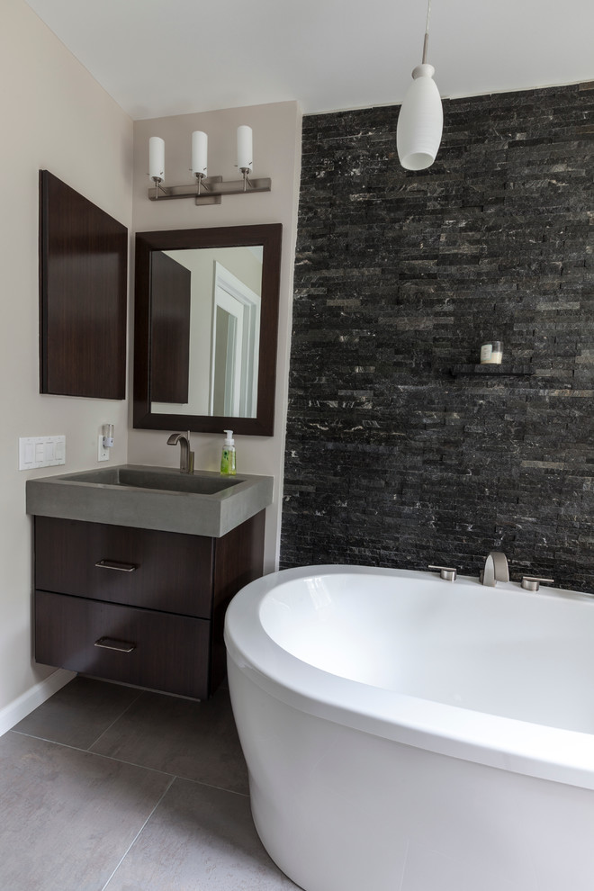 Inspiration for a large industrial ensuite bathroom in Bridgeport with an integrated sink, flat-panel cabinets, dark wood cabinets, concrete worktops, a freestanding bath, an alcove shower, a two-piece toilet, grey tiles, porcelain tiles, grey walls and porcelain flooring.