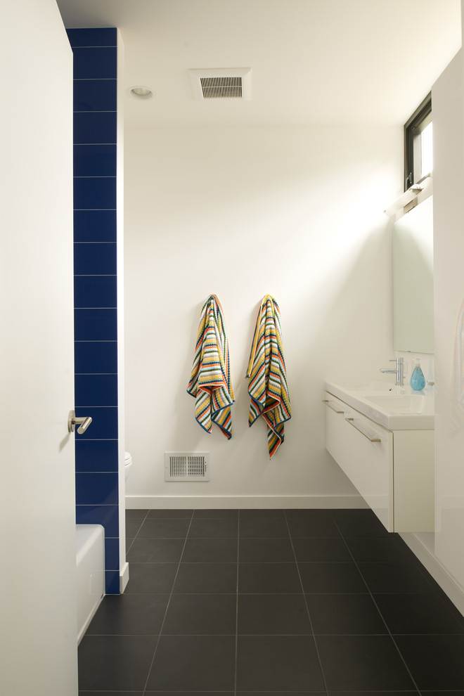 Cette photo montre une salle de bain moderne pour enfant avec des portes de placard blanches et un carrelage gris.