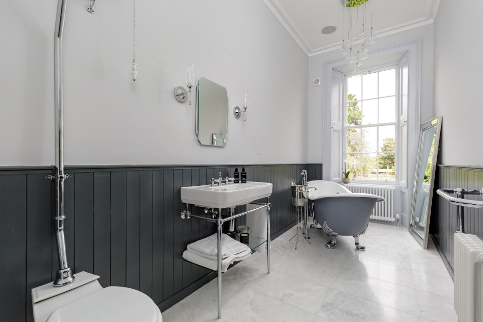 Пример оригинального дизайна: ванная комната в классическом стиле с ванной на ножках, белыми стенами, консольной раковиной, серым полом, тумбой под одну раковину и панелями на стенах
