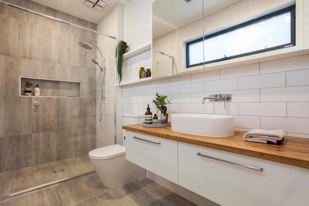 Идея дизайна: ванная комната среднего размера в морском стиле с плоскими фасадами, белыми фасадами, угловым душем, раздельным унитазом, белой плиткой, плиткой кабанчик, настольной раковиной, столешницей из дерева и душем с распашными дверями