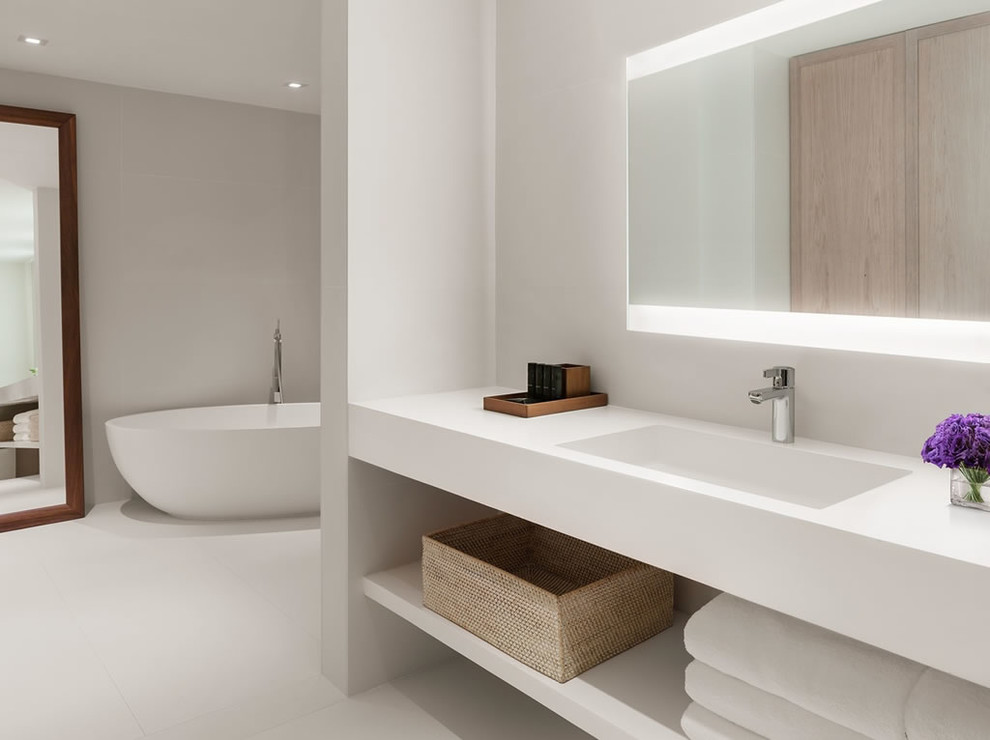 Cette photo montre une grande salle de bain principale chic avec un placard sans porte, une baignoire indépendante, un mur blanc, un plan de toilette en surface solide et un sol blanc.