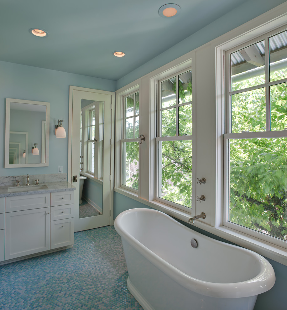На фото: главная ванная комната среднего размера в стиле неоклассика (современная классика) с фасадами в стиле шейкер, белыми фасадами, отдельно стоящей ванной, синими стенами, полом из керамогранита, врезной раковиной, мраморной столешницей и синим полом с