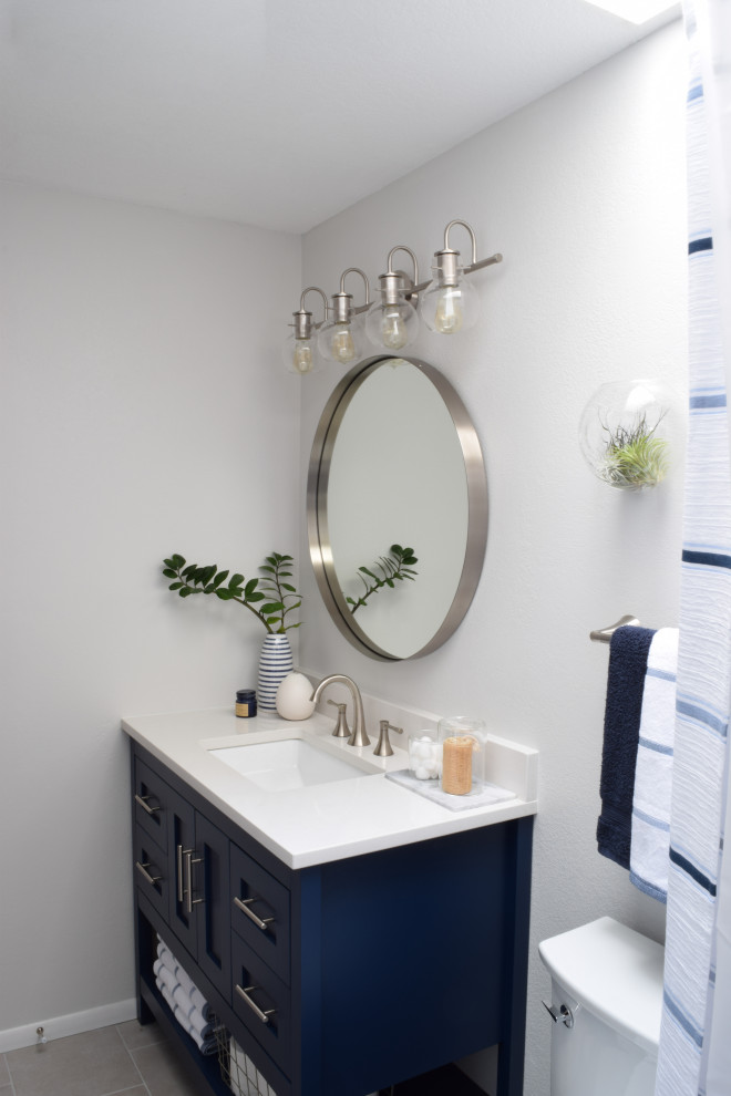 Exempel på ett mellanstort modernt vit vitt badrum, med skåp i shakerstil, blå skåp, ett badkar i en alkov, en dusch/badkar-kombination, en toalettstol med separat cisternkåpa, vit kakel, tunnelbanekakel, vita väggar, kalkstensgolv, ett undermonterad handfat, bänkskiva i akrylsten, grått golv och dusch med duschdraperi