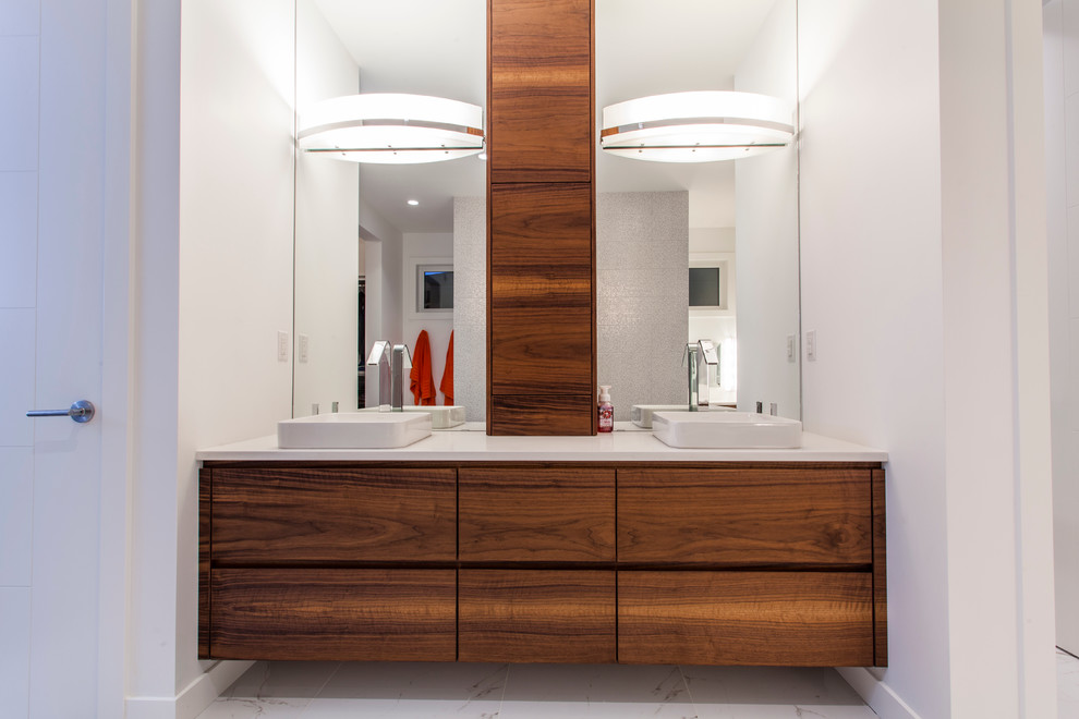 This is an example of a modern ensuite bathroom in Edmonton with a vessel sink, flat-panel cabinets, medium wood cabinets, quartz worktops, a freestanding bath, a double shower, white tiles, porcelain tiles, white walls and porcelain flooring.