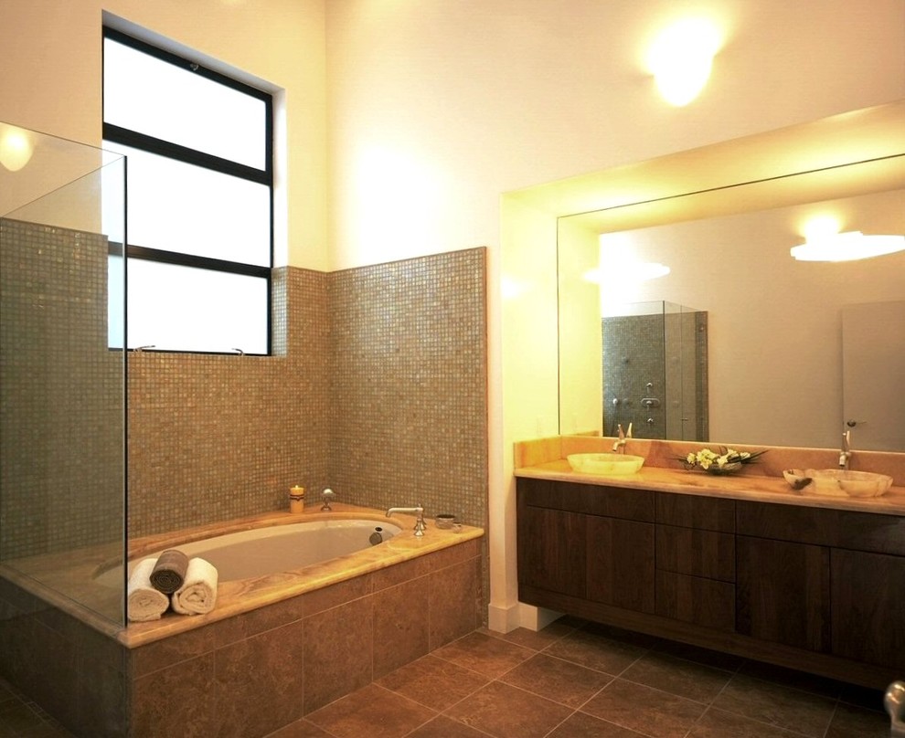 Идея дизайна: главная ванная комната в стиле модернизм с настольной раковиной, плоскими фасадами, темными деревянными фасадами, столешницей из оникса, полновстраиваемой ванной, душем над ванной, желтой плиткой, стеклянной плиткой, желтыми стенами и полом из травертина