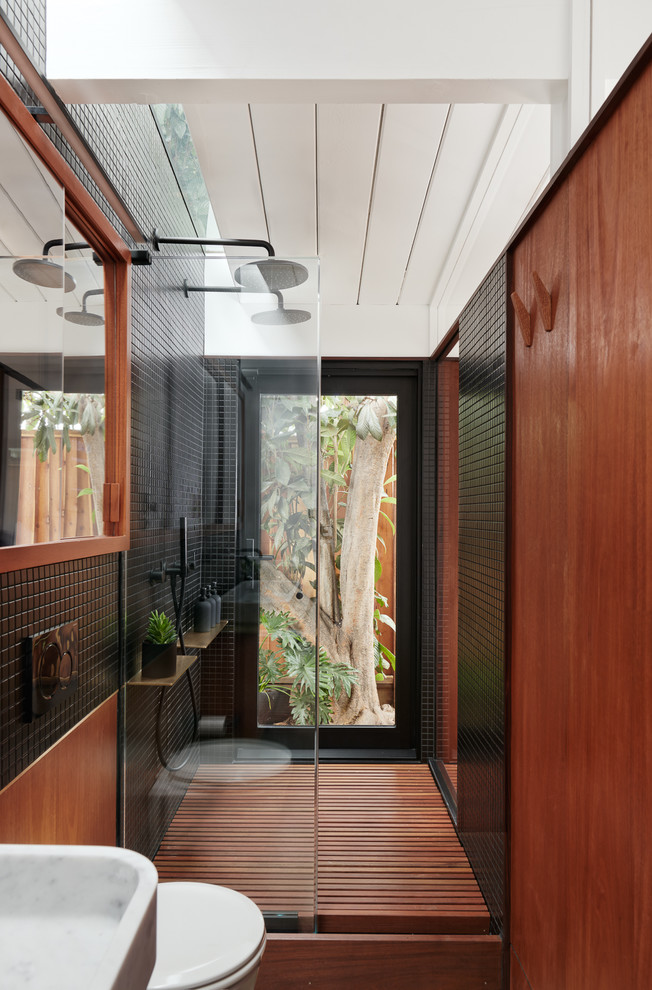 Asiatisk inredning av ett badrum med dusch, med en dubbeldusch, en toalettstol med hel cisternkåpa, svart kakel, bruna väggar och med dusch som är öppen