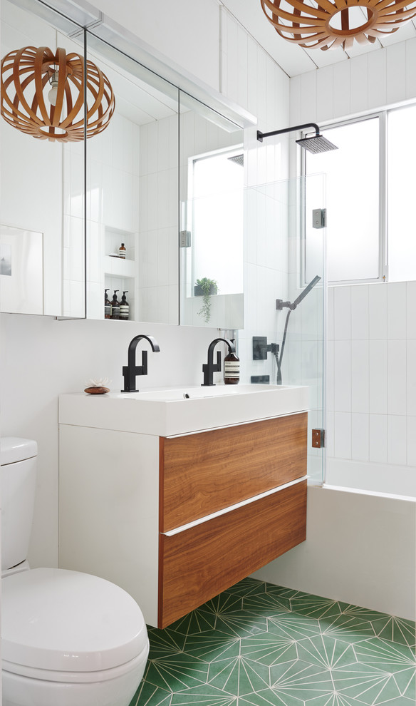 На фото: ванная комната в скандинавском стиле с плоскими фасадами, фасадами цвета дерева среднего тона, ванной в нише, душем над ванной, белой плиткой, белыми стенами, душевой кабиной, монолитной раковиной, зеленым полом, белой столешницей и окном с