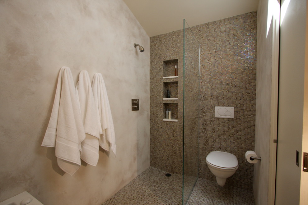 Inspiration för ett mellanstort funkis en-suite badrum, med ett fristående handfat, släta luckor, skåp i mörkt trä, bänkskiva i akrylsten, ett badkar i en alkov, en kantlös dusch, en vägghängd toalettstol, flerfärgad kakel, mosaik, beige väggar och mosaikgolv